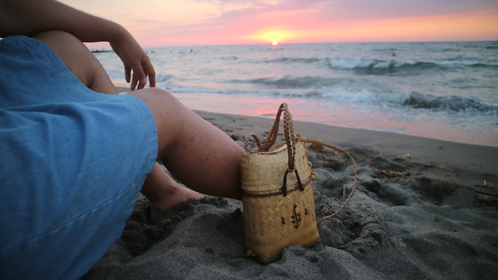 Persona in pantaloncini blu che si siede sul secchio marrone sulla spiaggia durante il giorno