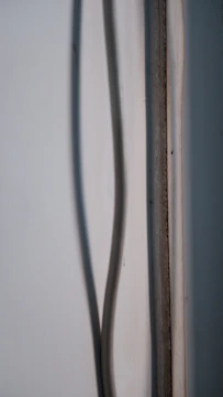A close-up view of a wall with a light-colored cable running vertically along it. The cable creates a shadow on the wall. The wall and cable have a slightly worn and aged appearance.