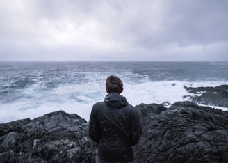 A person standing strong on a rocky cliff facing a storm, symbolizing resilience.
