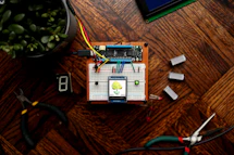Hands programming a home automation device surrounded by green plants and electronic parts.