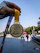 A hand holding a gold medal with the inscription 'Tata Mumbai Marathon 2020' is prominently displayed against a background of a marathon event, showcasing participants running on a city street. The medal's design features an embossed runner and text highlighting the marathon's completion distance.
