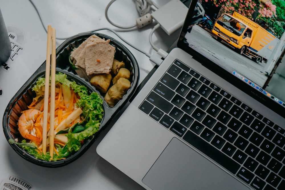 Black ceramic bowl with Asian food next to a laptop.
