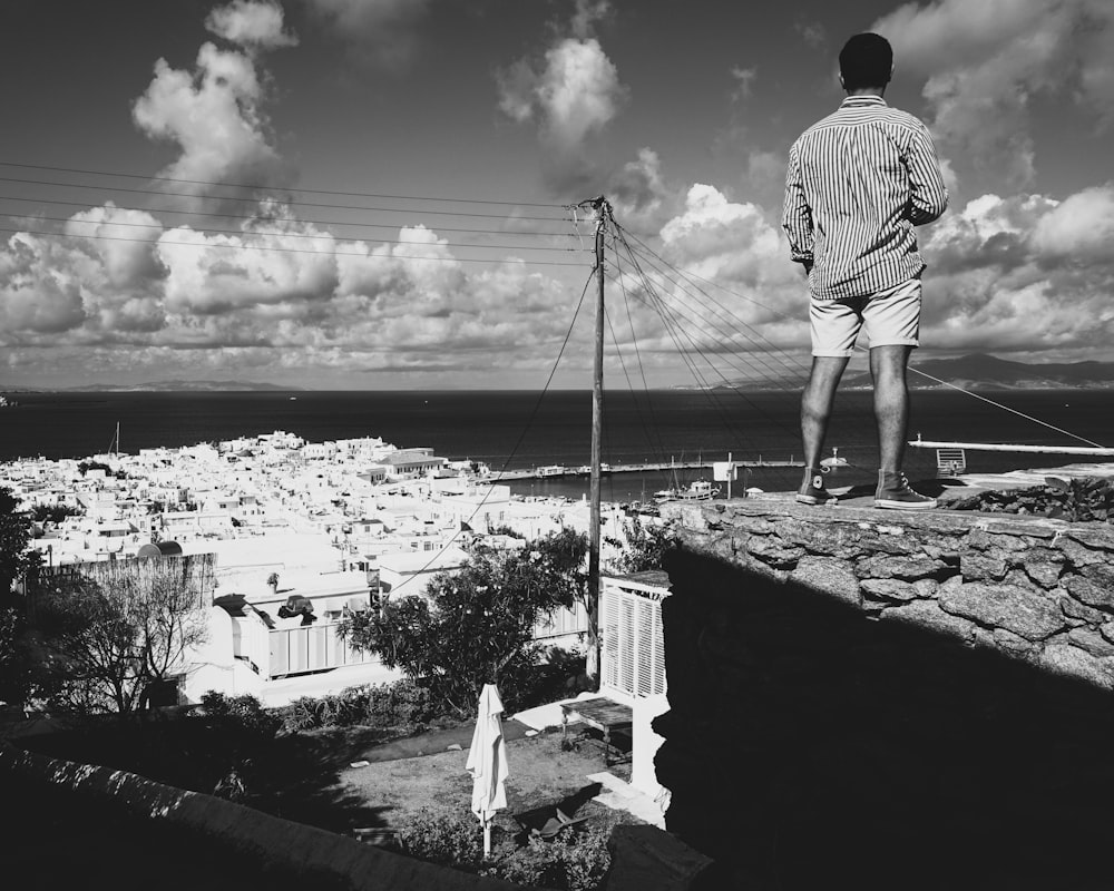 man in white long sleeve shirt and white pants standing on rock near body of water