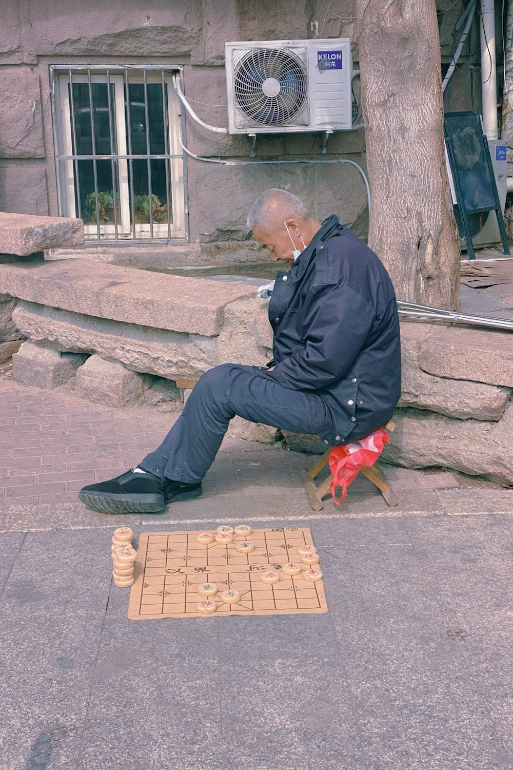 man in black jacket and black pants sitting on concrete bench beside brown short coated dog