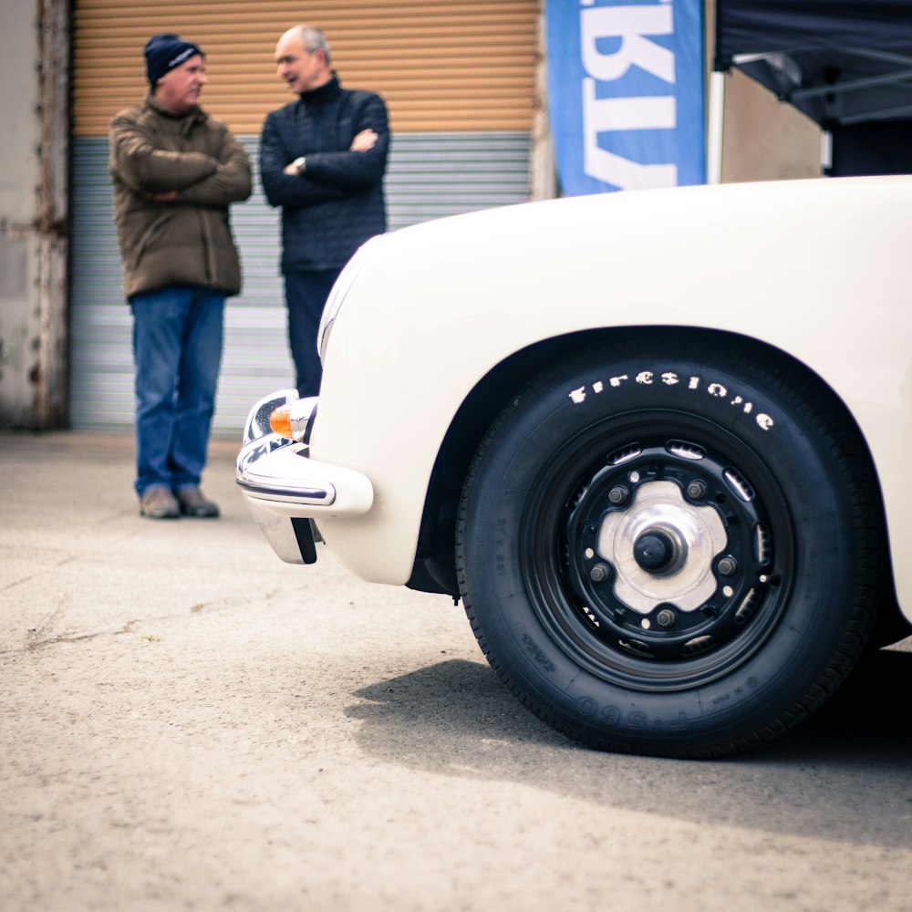 man in black jacket and blue denim jeans standing beside white car