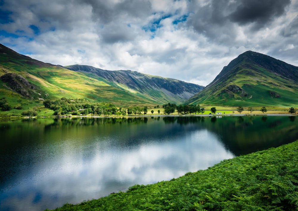 green mountains beside lake under cloudy sky during daytime