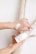 Hands are applying a white cream from a container labeled 'nora Eczema Hydro Cream' onto the skin. The background consists of light-colored wooden branches.