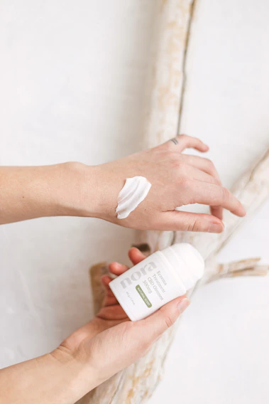 Close-up of a hand gently applying soothing cream from a small jar labeled 'hopewave' on dry skin.