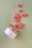 A tipped-over jar labeled 'nora Flavored CBD Gummies' scatters red gummies across a light green surface. The gummies are small, circular, and have a sugar coating.