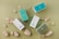 Several rectangular boxes with product labels, placed among natural coral stones on a green surface. The boxes have a minimalist design with colors like teal, light blue, white, and muted green.
