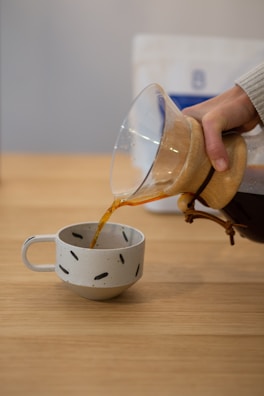 Hand pouring coffee into a ceramic cup on a wooden table