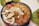 A sizzling hotpot filled with a variety of ingredients including shrimp, mushrooms, quail eggs, meatballs, and abalone. The dish is rich in colors and textures, steaming hot and ready to serve. The background shows a leafy serving plate with additional food items.