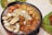 A sizzling hotpot filled with a variety of ingredients including shrimp, mushrooms, quail eggs, meatballs, and abalone. The dish is rich in colors and textures, steaming hot and ready to serve. The background shows a leafy serving plate with additional food items.