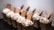 A row of desserts in clear cups, each featuring a layer of creamy pudding topped with whipped cream, a biscuit, and chocolate pieces. The presentation is neat and appealing, with the desserts aligned on a dark surface.