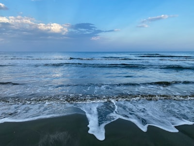 Soft waves lapping a quiet sandy shore under a calm blue sky.