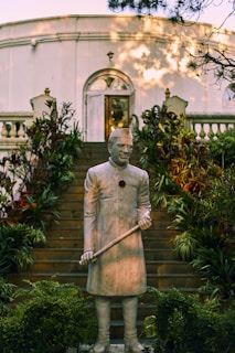 man holding stick statue near green plants during daytime