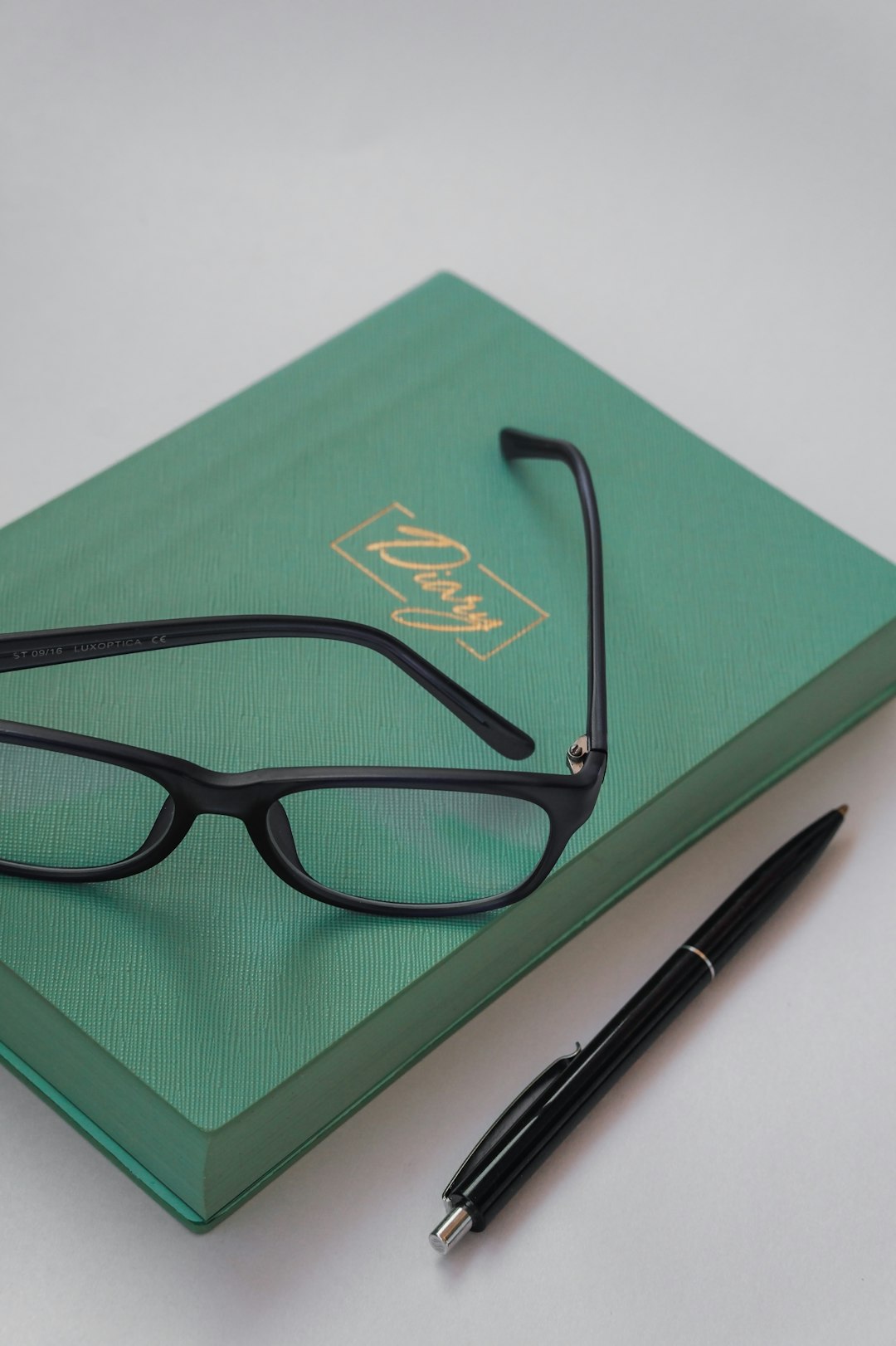 black framed eyeglasses beside black click pen on green book