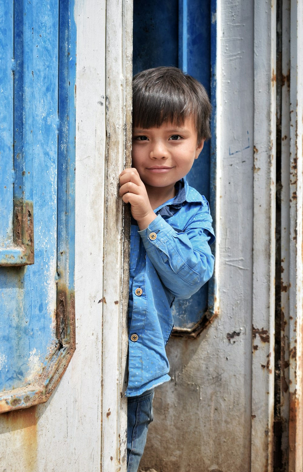 boy in blue denim jacket standing beside blue wooden door