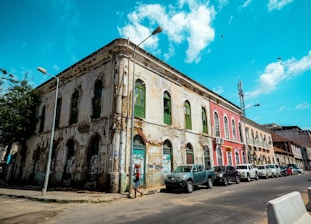 cars parked in front of brown concrete building under blue sky and white clouds during daytime