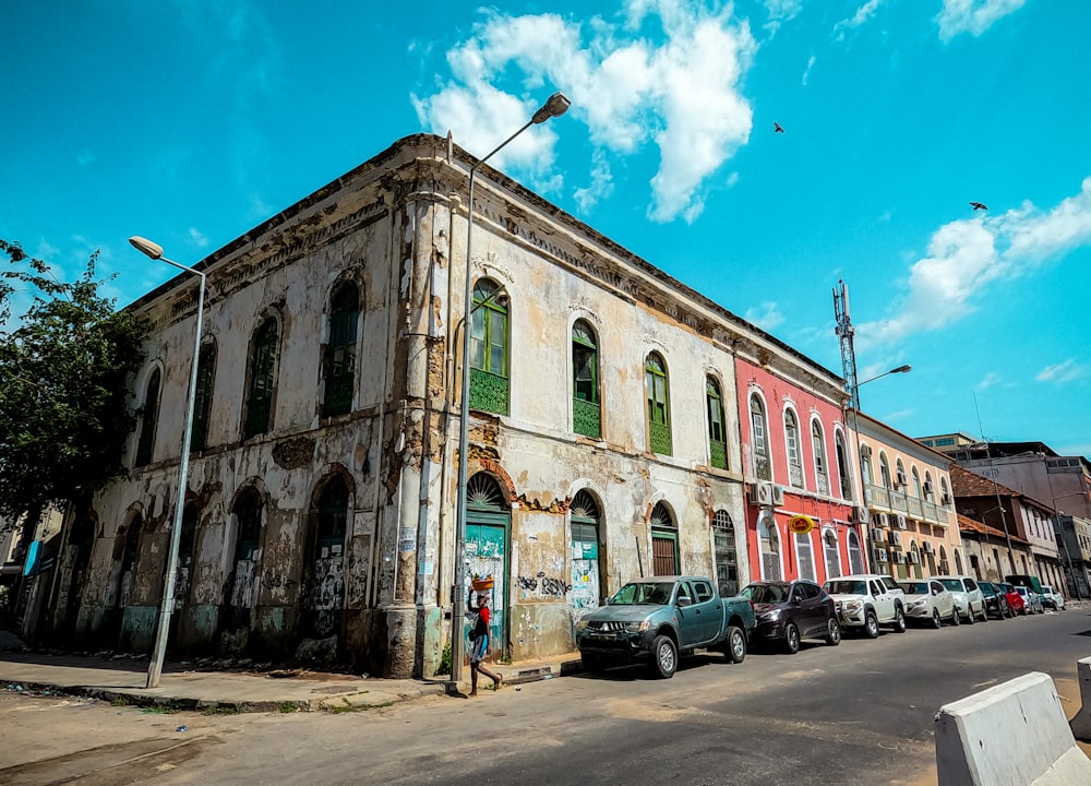 cars parked in front of brown concrete building under blue sky and white clouds during daytime