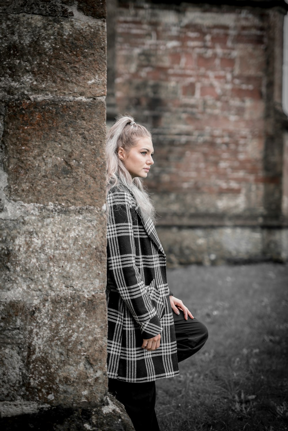 woman in black and white plaid coat standing beside brown concrete wall during daytime