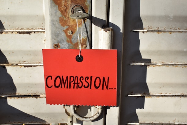 A red card with the word 'COMPASSION...' written in large black letters is attached to a metal latch on a weathered, rusted door.