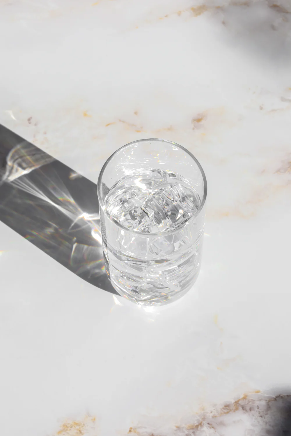 A clear glass of water on a white table in strong sunlight.
