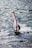 A windsurfer skillfully navigates the choppy waters, balancing on a board with a red and white sail. The sunlight reflects off the waves, creating a shimmering effect on the surface of the sea.