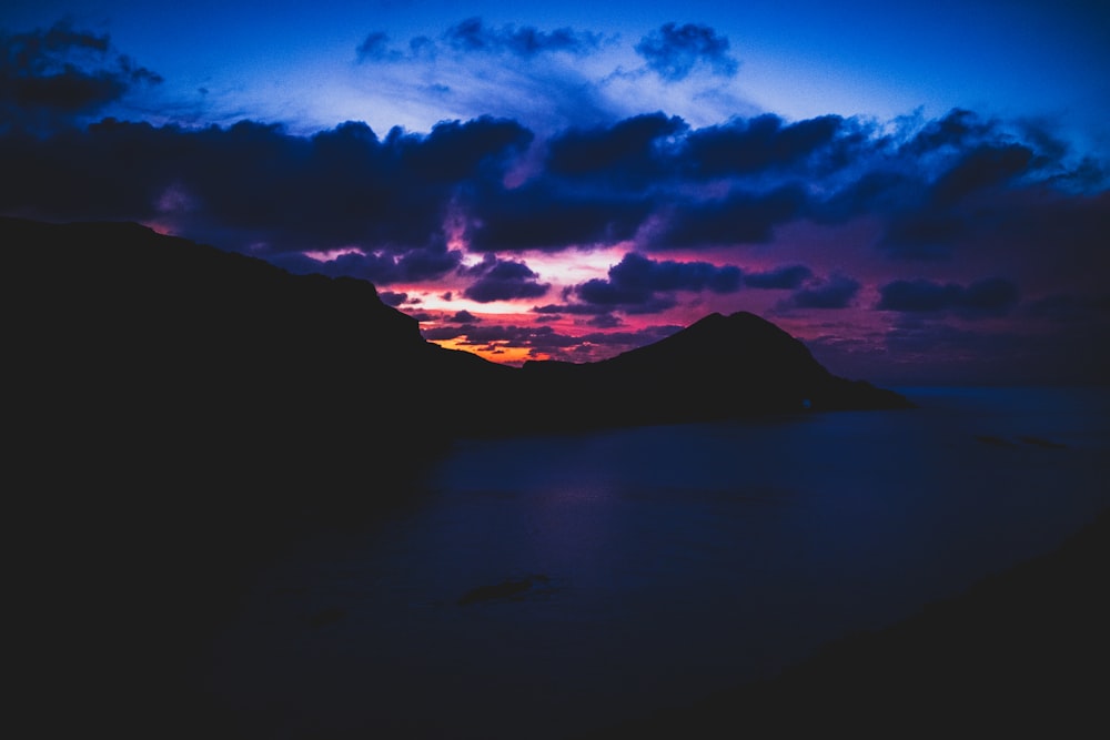 silhouette of mountain under cloudy sky during night time