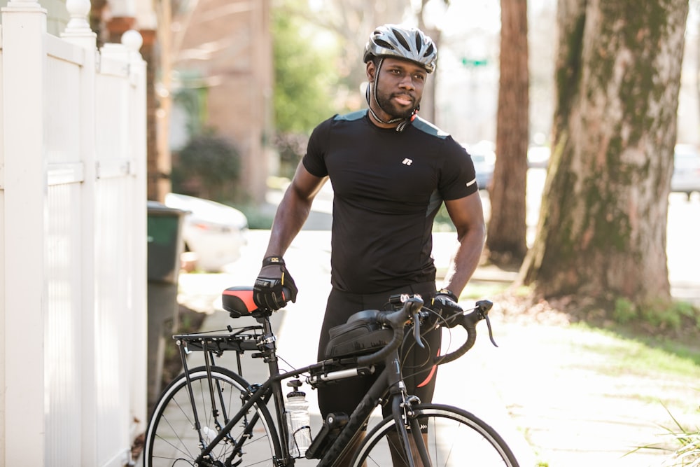 Homme en T-shirt à col rond noir et casque blanc roulant sur un vélo noir pendant la journée