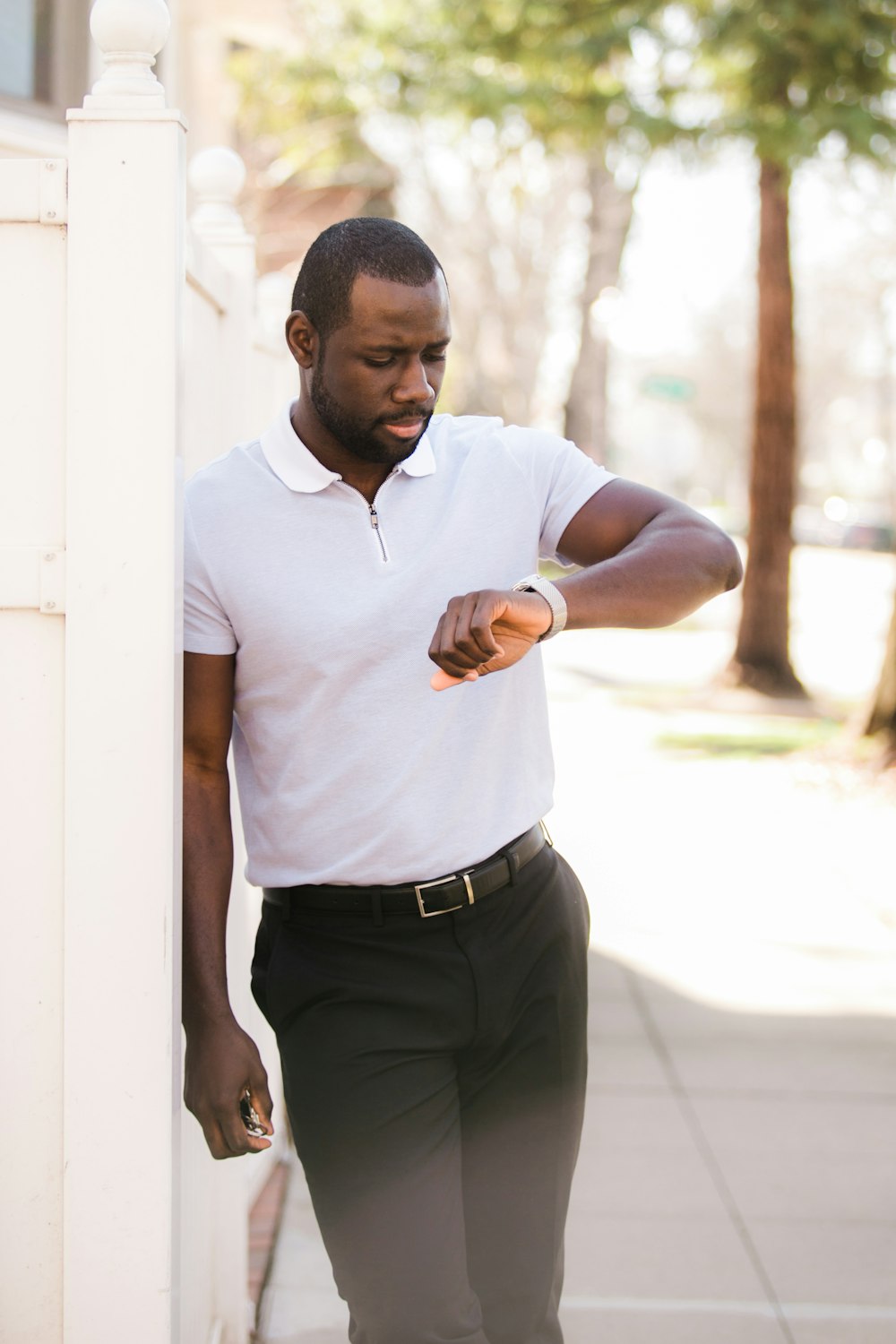 man in white polo shirt and black pants standing near white wall during daytime