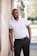 man in white polo shirt and black pants standing beside white wall during daytime