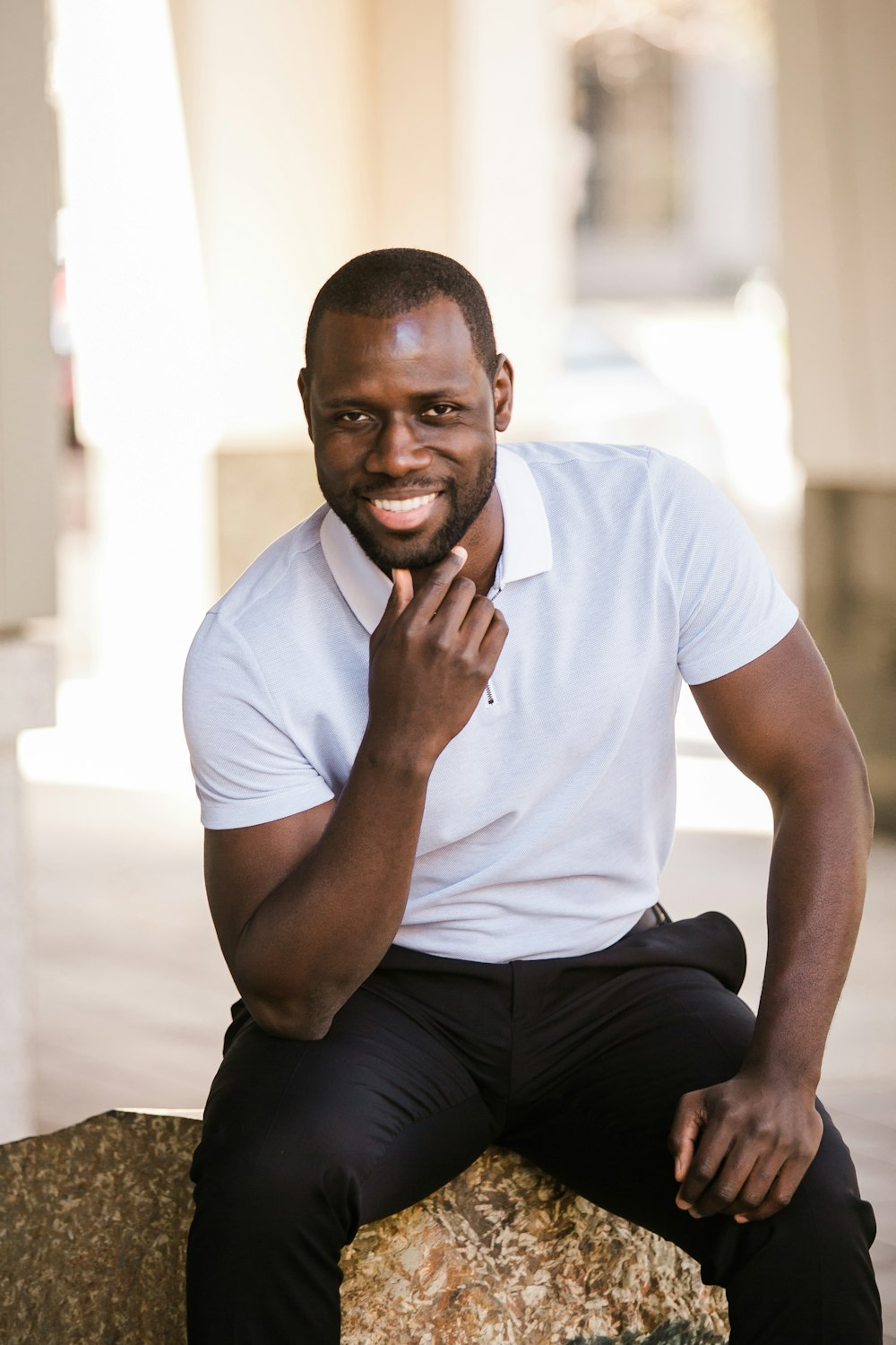 man in white crew neck t-shirt and black pants sitting on white concrete wall during