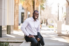 man in white dress shirt and black pants sitting on the sidewalk during daytime