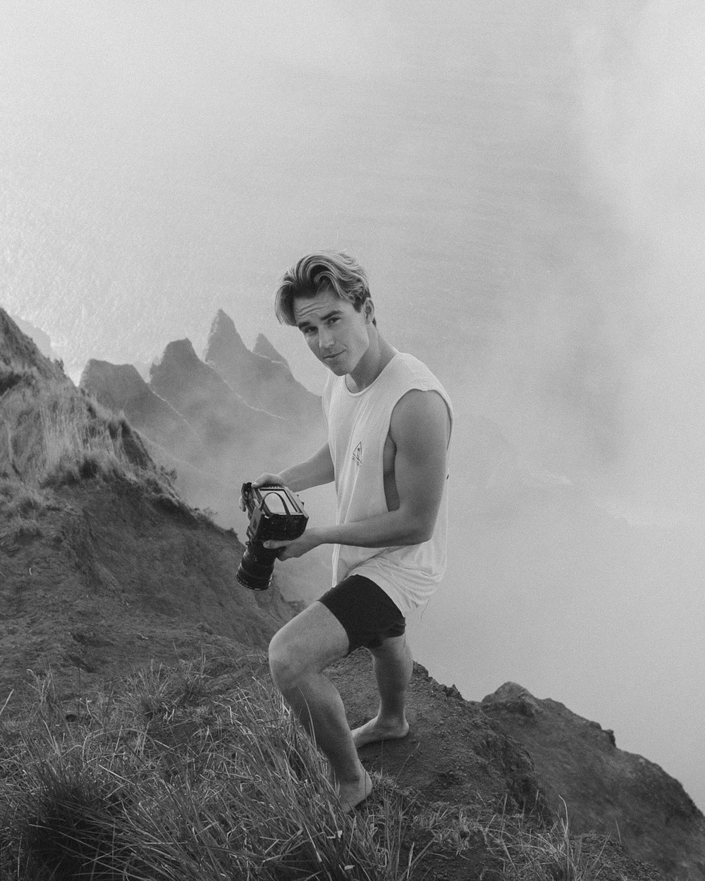 man in tank top and shorts sitting on rock