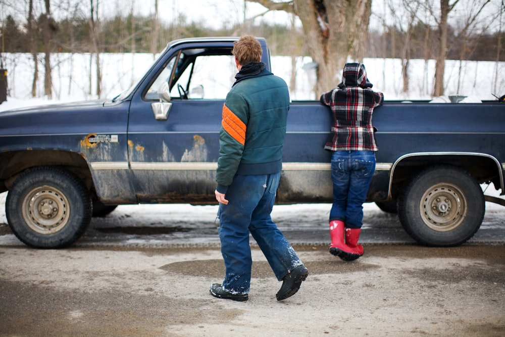 man in blue jacket and blue denim jeans standing beside black car during daytime