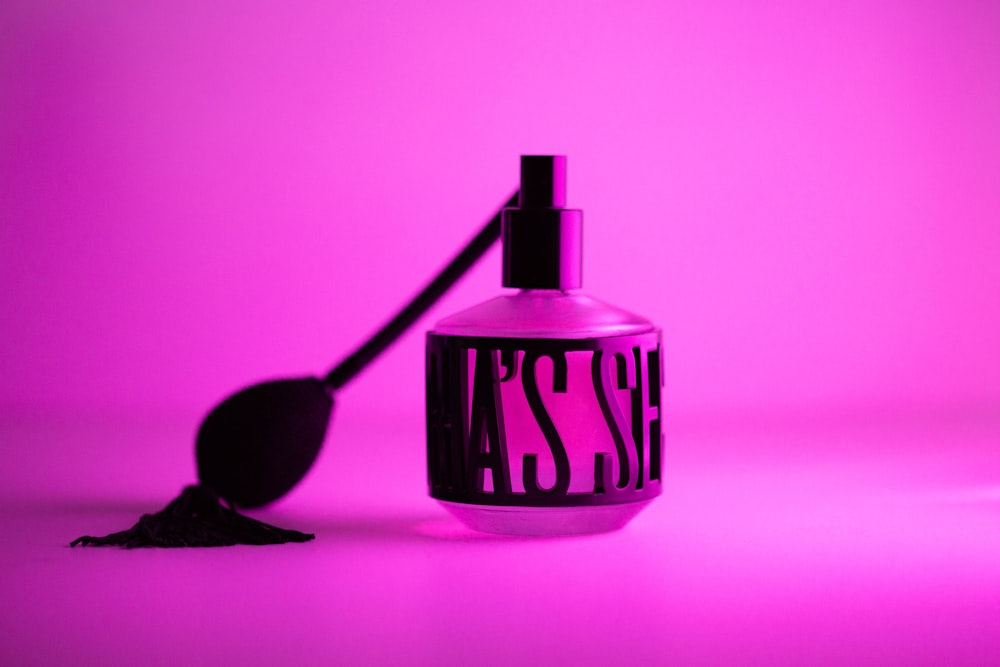 a bottle with a spoon next to it on a pink background