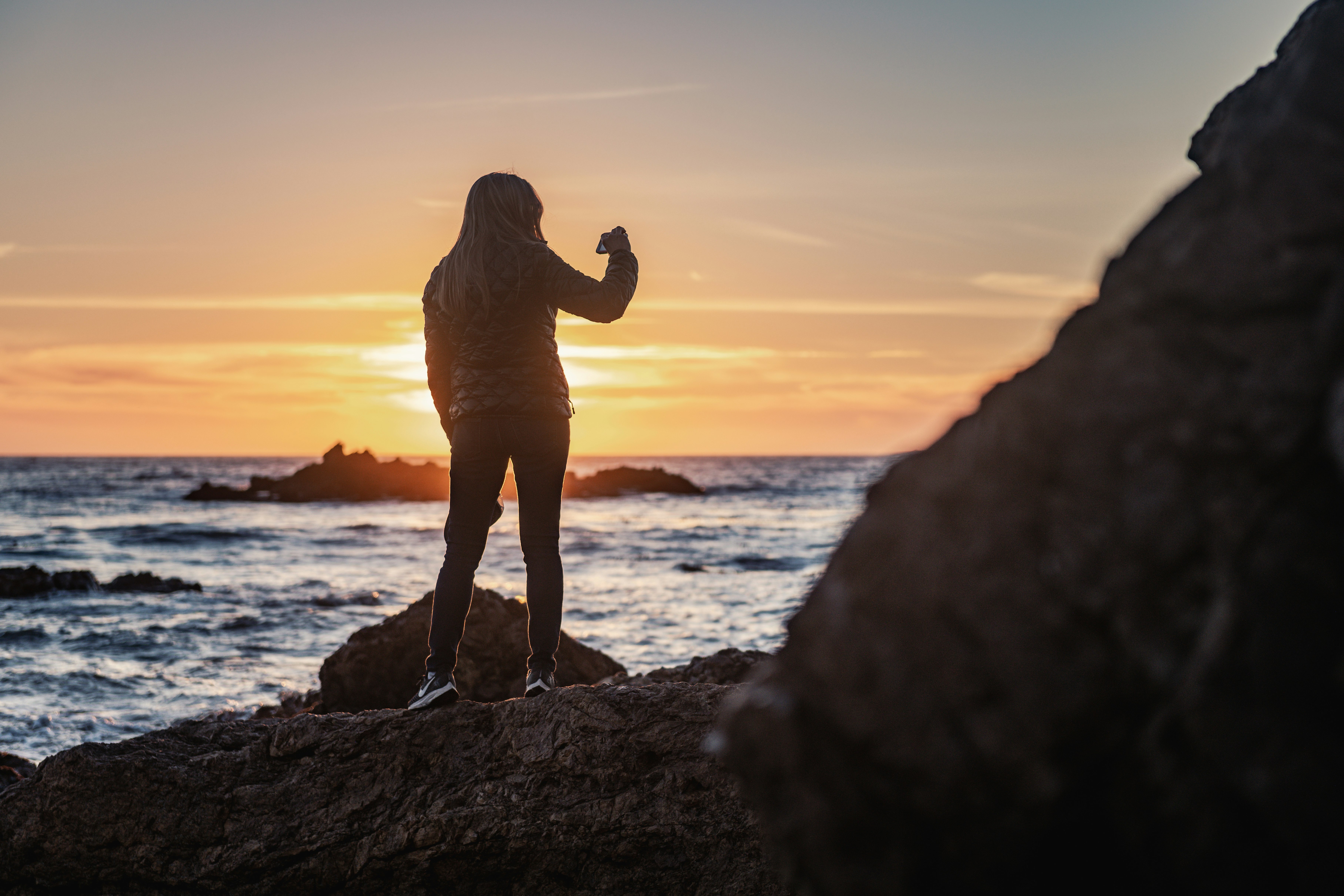 silhouette of man standing on rock near body of water during sunset