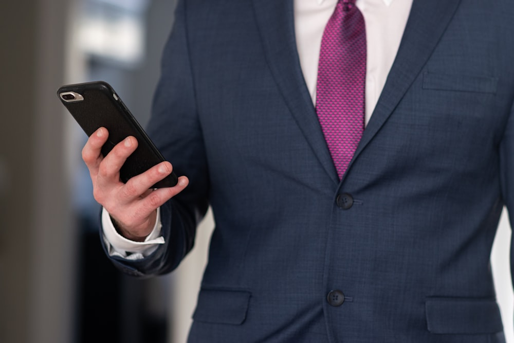 man in black suit jacket holding black smartphone