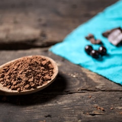 Wooden spoon full of cocoa powder styled over table top with chocolate & coffee cherries