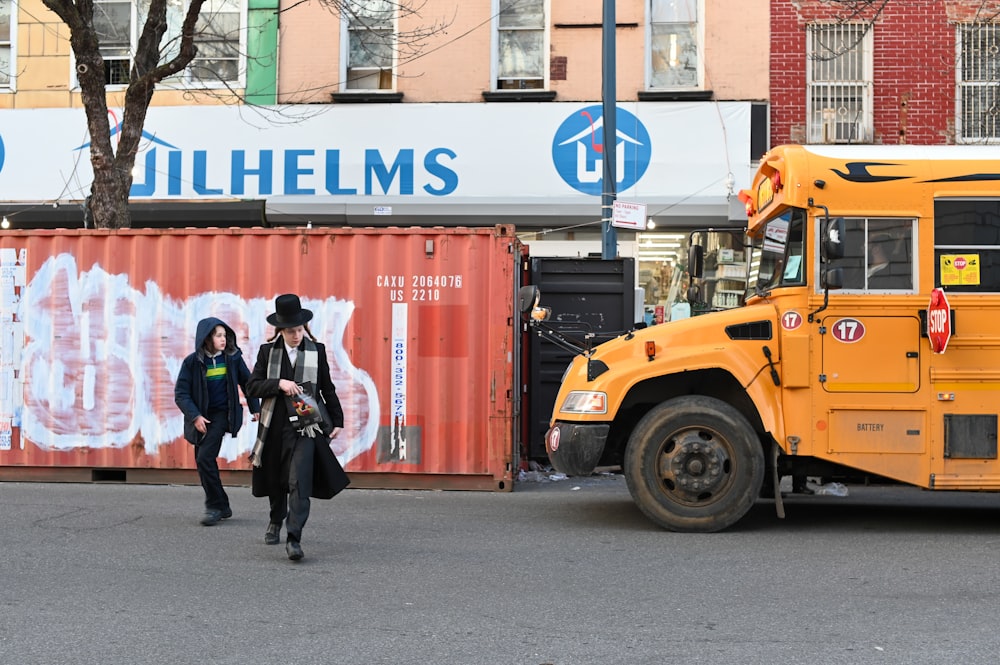 man in black jacket and black pants standing beside yellow truck during daytime