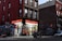 A corner deli with a brightly lit storefront displays various snacks and drinks inside. The exterior features vibrant street art and graffiti covering the adjacent brick walls. A few bicycles are parked nearby, and an evening urban environment is evident from the dim street lighting.