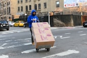 man in blue hoodie holding brown cardboard box