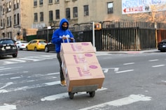 man in blue hoodie holding brown cardboard box
