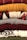 A stack of neatly folded knitted sweaters with various textures and patterns, showing a range of colors from deep red and mustard yellow to gray, burgundy, and patterned white and black. The fibers and knitting patterns are clearly visible, emphasizing the cozy and warm nature of the garments.