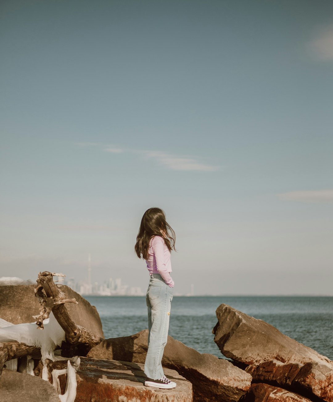 woman in white tank top and blue denim jeans standing on brown rock formation near sea