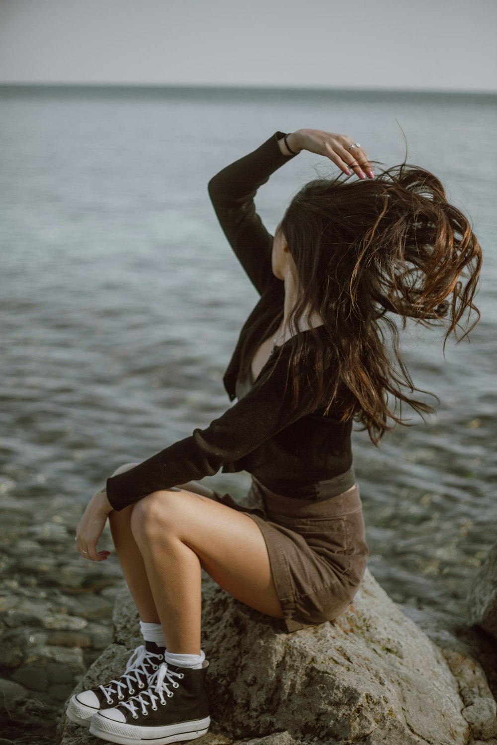 woman in black long sleeve shirt and brown shorts sitting on brown sand during daytime