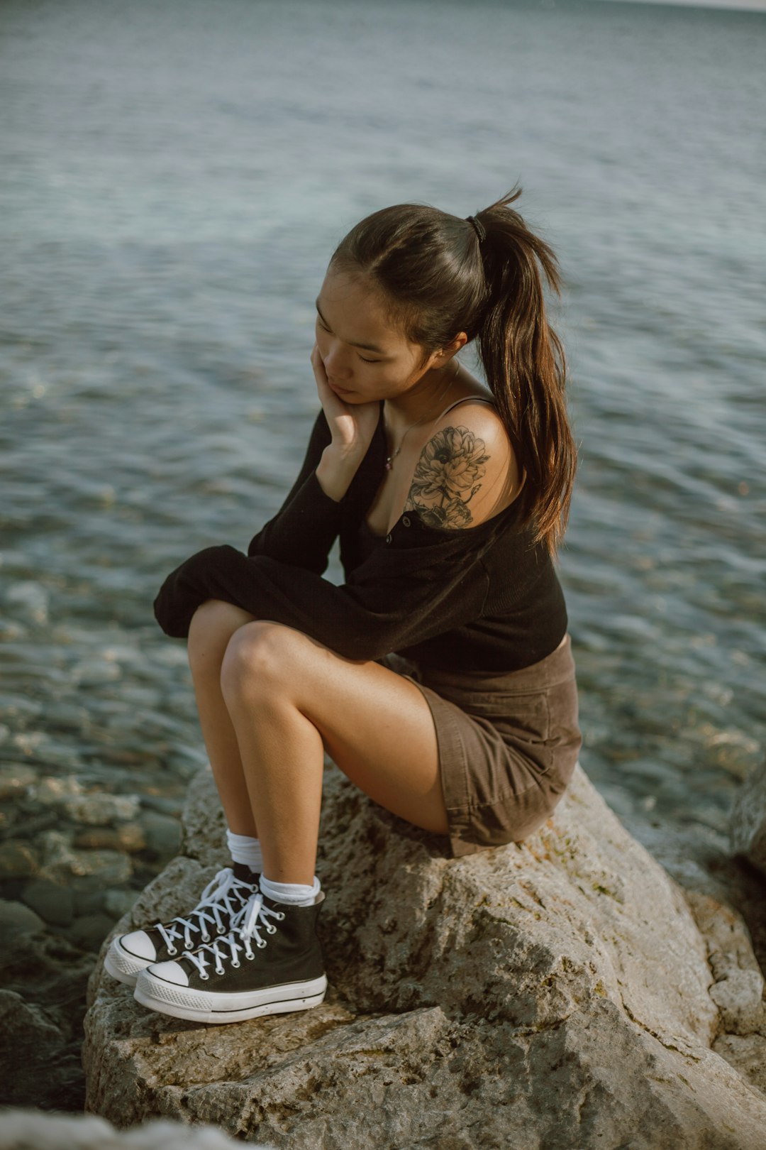 woman in black long sleeve shirt and black and white shorts sitting on rock near body