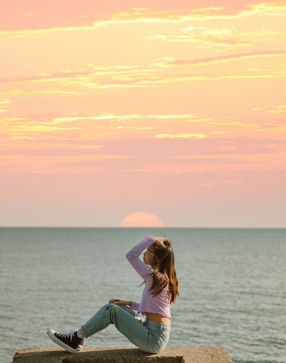 woman in white shirt and blue denim jeans sitting on blue and white boat during sunset