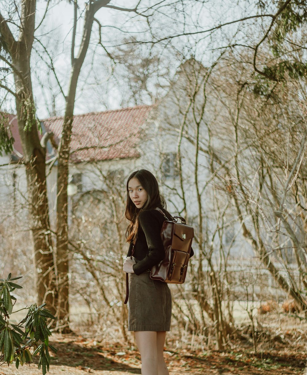 woman in black long sleeve shirt and brown skirt standing near brown tree during daytime